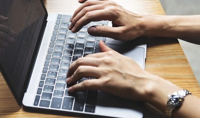 Laptop keyboard with hands typing on a wooden desk, modern work environment, technology, productivity, remote work.