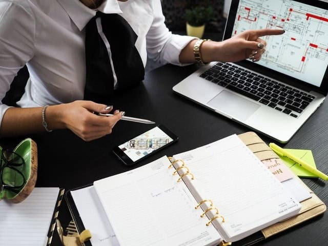 Blueprint architectural design on laptop screen with business planner and smartphone on desk.
